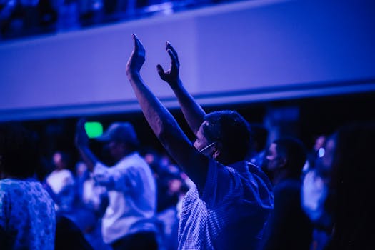 Audience in blue lighting with raised hands at an event, capturing lively energy.