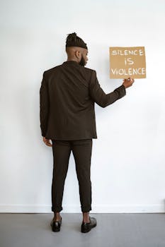 Man in tailored suit holds sign saying 'Silence is Violence'