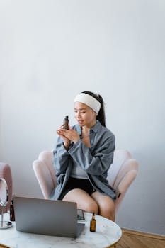 Young woman with headband reviews beauty products at home using laptop.